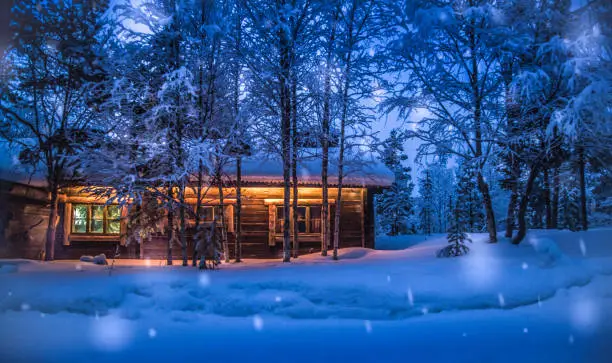 Romantic view of old traditional wooden forest cabin in the woods embedded in scenic northern winter wonderland scenery in beautiful mystic twilight during blue hour at dusk