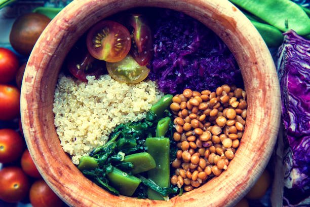 Buddha bowl with quinoa, cherry tomatoes, red cabbage, lentils, green beans and spinach in a wooden bowl and vegetables around.