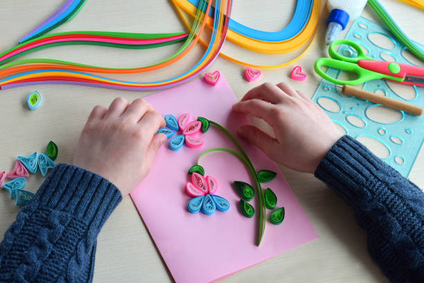 istock Quilling technique. Boy making decorations or greeting card. Paper strips, flower, scissors. Handmade crafts on holiday: Birthday, Mother's or Father's Day, March 8, Wedding. Children's DIY concept. 928388400