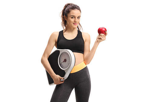 Fitness woman holding a weight scale and an apple isolated on white background