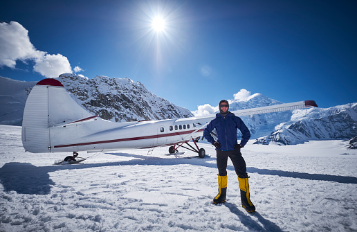 Snow Plane Landing on Ruth Glacier in Denali National Park. On a beautiful sunny day with the mountains in de background. One of the mountaineers poses in front of the plane on the glaciers