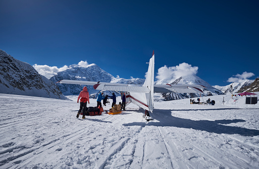 Snow Plane Landing on Ruth Glacier in Denali National Park. On a beautiful sunny day with the mountains in de background. A number of men take the baggage from the plane what they need for the expedition on Denali.