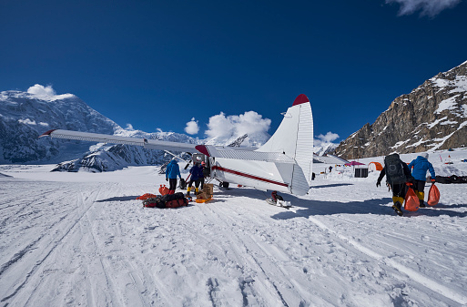 Snow Plane Landing on Ruth Glacier in Denali National Park. On a beautiful sunny day with the mountains in de background. A number of men take the baggage from the plane what they need for the expedition on Denali.