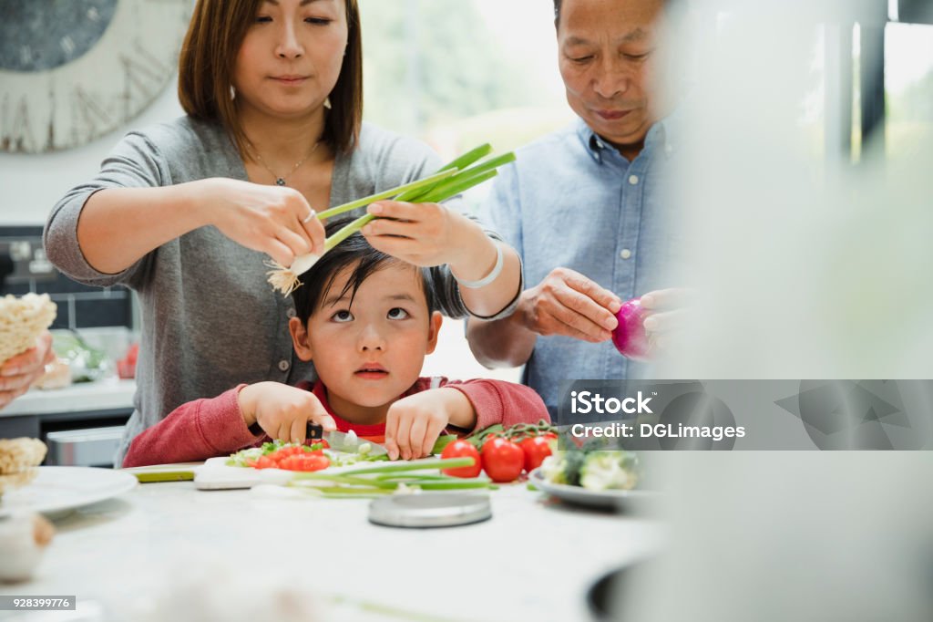 Learning to Make a Stir Fry with my Grandparents Little boy is learning how to prepare vegetables with his family who are making a stir fry. He is chopping spring onions and tomatoes. Family Stock Photo