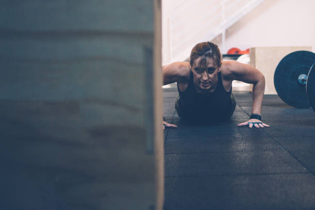 Girl doing burpees Close up of a young athlete woman doing burpees on a gym workout at the box gym. Copy space area available burpee stock pictures, royalty-free photos & images