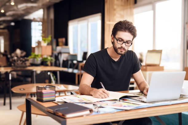 istock Freelancer bearded man taking notes at laptop sitting at desk. 928404628