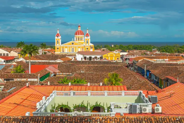 The complete urban skyline of Granada with its striking yellow cathedral, rooftops in Spanish colonial style architecture and the Nicaragua lake in the background, Nicaragua, Central America.