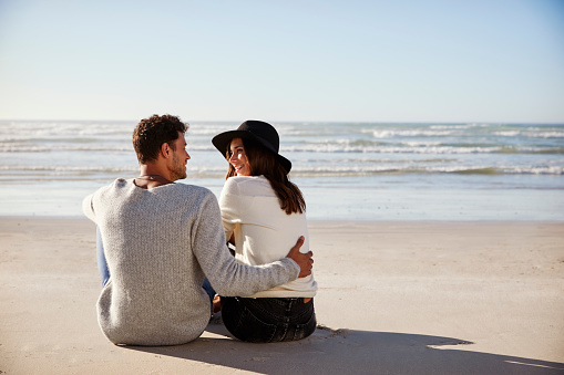 Romantic Couple Sitting On Winter Beach Together