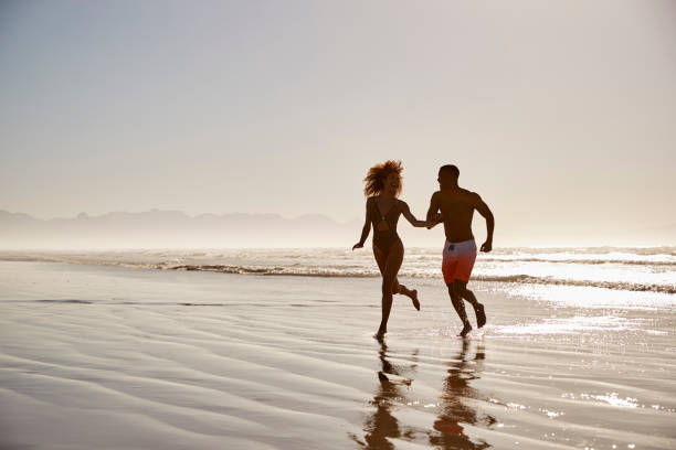 istock Couple Having Fun Running Through Waves On Beach Vacation 928410732