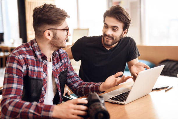 istock Two freelancer men looking at photos at laptop at desk. 928410852