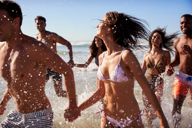 istock Group Of Friends Run Through Waves Together On Beach Vacation 928410934