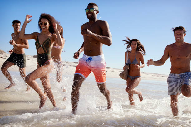 istock Group Of Friends Run Through Waves Together On Beach Vacation 928411108