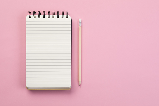 Spiral notebook and pencil on pink background
