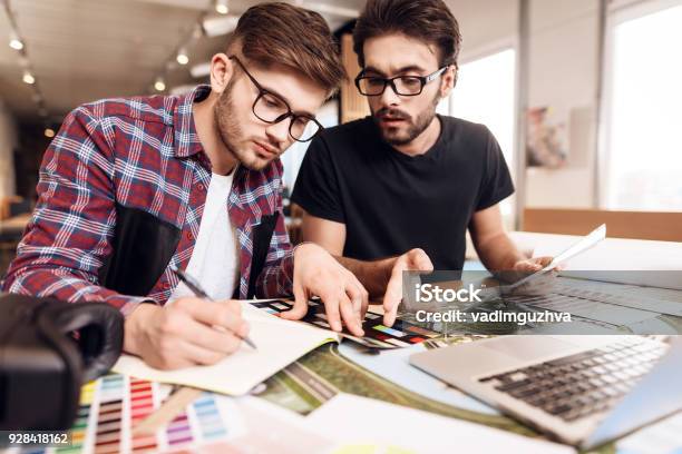 Two Freelancer Men Looking At Color Swatches At Laptop At Desk Stock Photo - Download Image Now