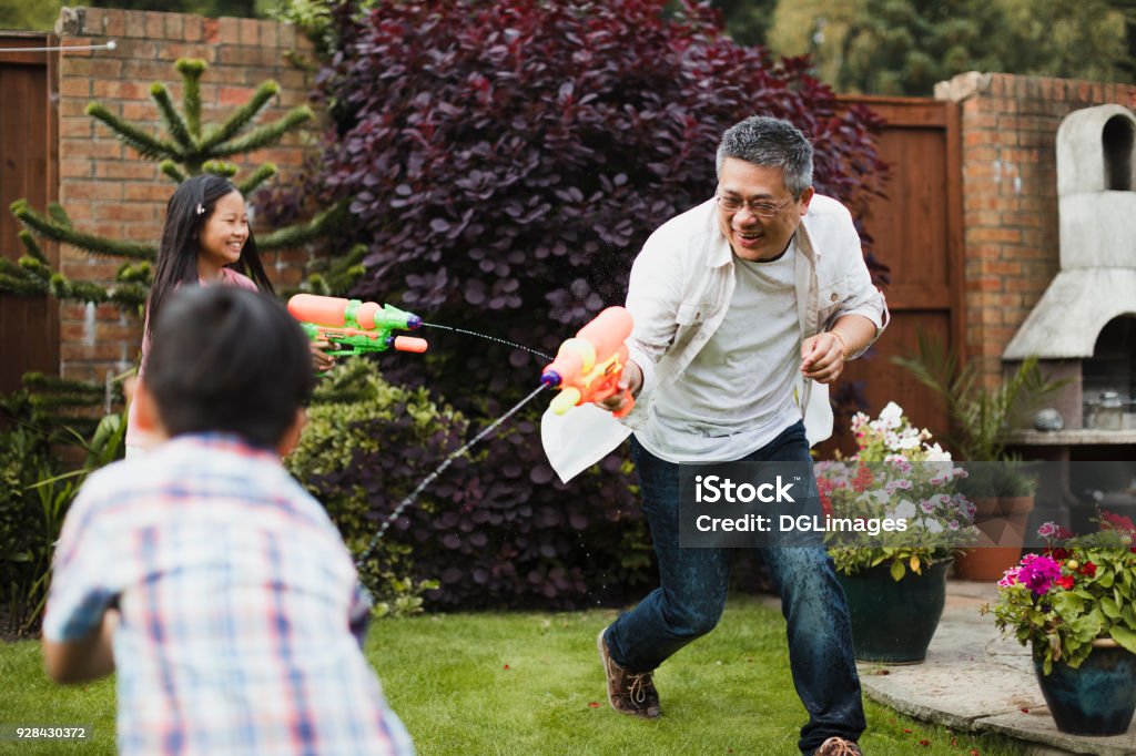 Family Having a Water Fight Family are having a water fight together with water pistols in the garden. The little girl is aiming for her dad, who is aiming for the little boy. Family Stock Photo