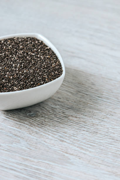istock Vertical image of chia seeds in a white ceramic bowl on a wooden table. 928441992