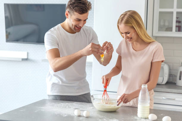 beau jeune couple cuisson déjeuner ensemble dans la cuisine le matin week-end - two eggs photos et images de collection