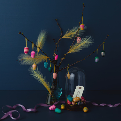 Easter still life with twigs and egg decorations with cruelty free artificial feathers on dark blue