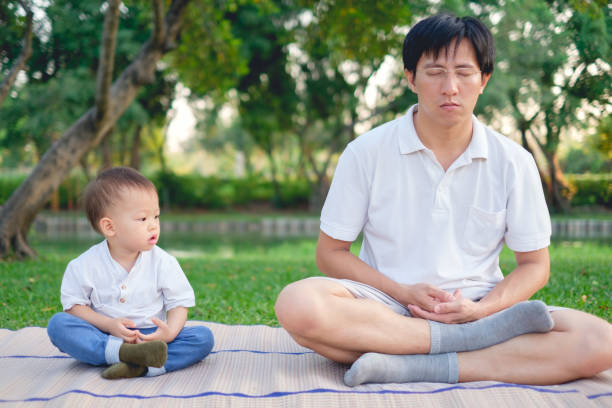отец с закрытыми глазами и симпатичные маленькие азиатские 18 месяцев / 1 год малыш мальчик ребенок практикует йогу и медитирует на открытом  - child exercising little boys toddler стоковые фото и изображения
