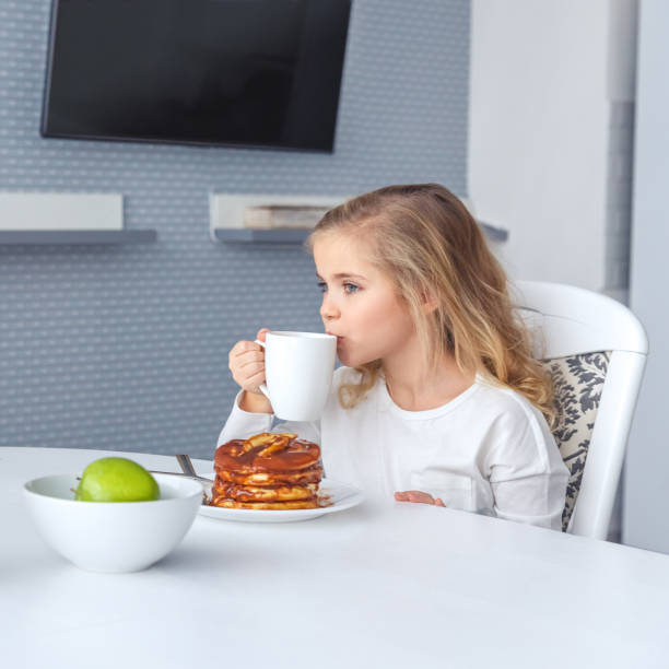little child having pancakes with tea for breakfast