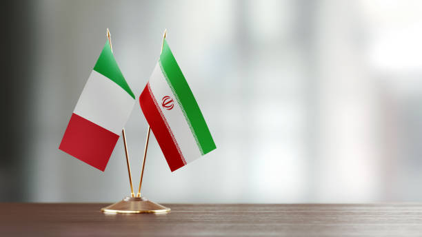 istock Italian And Iranian Flag Pair On A Desk Over Defocused Background 928478228