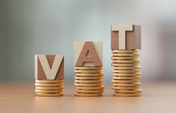 Cube Blocks And Coins Forming VAT Text Over Defocused Background Cube blocks made of wood material are standing on coin towers to form VAT text over defocused background. Horizontal composition with copy space. Great use for finance concepts. vat stock pictures, royalty-free photos & images