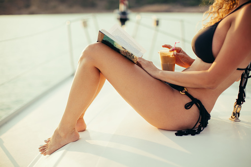 Beautiful woman with curly hair enjoying and sunbathing on sailboat at summer