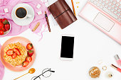 Beautiful flatlay arrangement with cup of coffee, hot waffles with cream and berries, laptop, smartphone with copyspace and other accessories: concept of busy morning breakfast, white background.