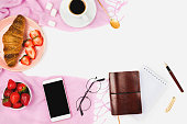 Beautiful flatlay arrangement with wholewheat croissant, cup of espresso coffee, fresh strawberries and business accessories: concept of busy morning or breakfast, white background. Copyspace