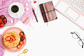 Beautiful flatlay arrangement with cup of coffee, hot waffles with cream and strawberries, laptop and other business accessories: concept of busy morning breakfast, white background.