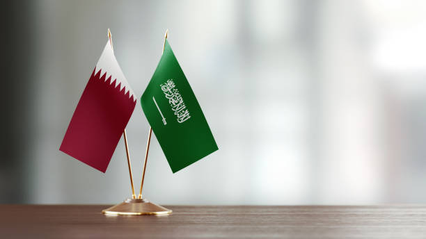 Qatari And Saudi Arabian Flag Pair On A Desk Over Defocused Background Qatari and Saudi Arabian flag pair on desk over defocused background. Horizontal composition with copy space and selective focus. qatar flag stock pictures, royalty-free photos & images