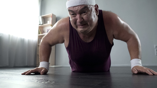 Motivated plump man in his 50s doing push-up with great effort, home training, stock footage