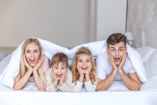 istock surprised young family lying in bed together under blanket and looking at camera 928506052