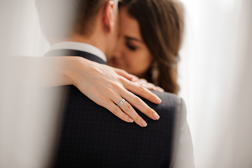 handsome bride brunette demonstrates her elegant diamond engagement ring on the bride's shoulder on a white background