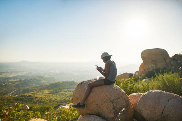 istock fit female hiker sitting on rock at mountain top using smartphone and relaxing 928549314