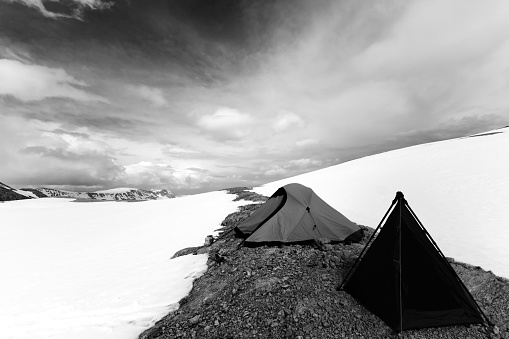 Two tents in snowy mountains. Turkey, Central Taurus Mountains, Aladaglar (Anti-Taurus), plateau Edigel (Yedi Goller). Wide angle view. Black and white toned image.
