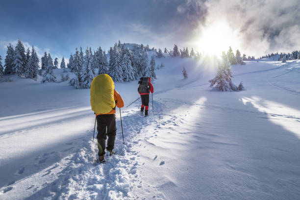 Two tourists climb the snow-covered winter mountain. Sunny weather and lots of snow around.