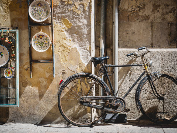 Old vintage bicycle leaning on a scratched wall with hanged decorated terracotta dishes. Landscape format.