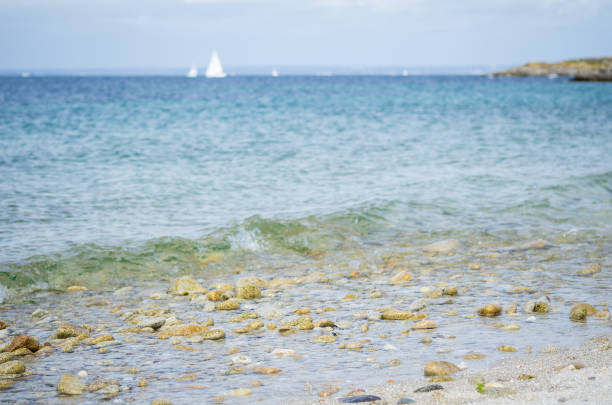Pebble beach, with blue sea and white boat in the background. Photographed in Glenan Isles (France)