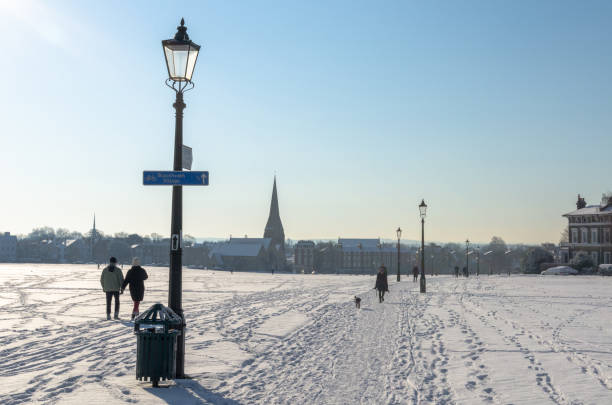 Couple and woman walking the dog at Blackheath Common. The All Saints Church and Blackheath village are in the background. Photo taken between Greenwich and Lewisham boroughs of London during the so called Beast from the East cold weather spell