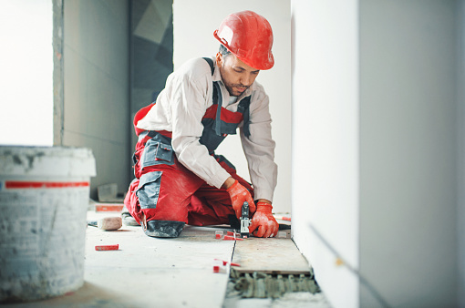 Closeup front view of a handyman installing  ceramic tiles over apartment floor. He's putting plastic crosses in the junction spot to keep the space between the tiles constant.