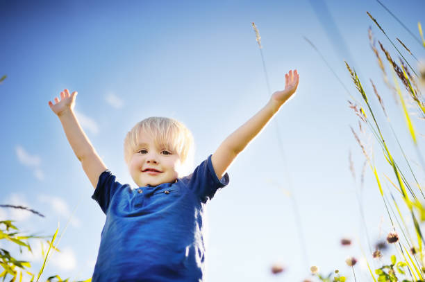 Cheerful little boy enjoying warm summer day. Active child playing in meadows. Freedom, rest and childhood concept. Happy kid outdoors