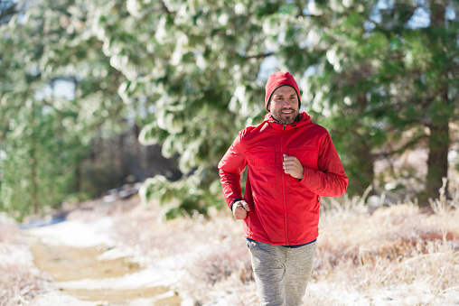 A man wearing red running through green pines trees