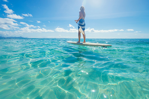 Woman paddling on a stand up paddleboard. She is wearing bikini in a tropical climate. Turquoise water in Fiji islands.