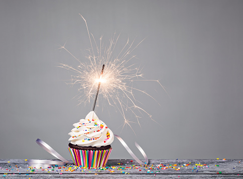 Cupcake with sprinkles and a sparkler over a gray background.