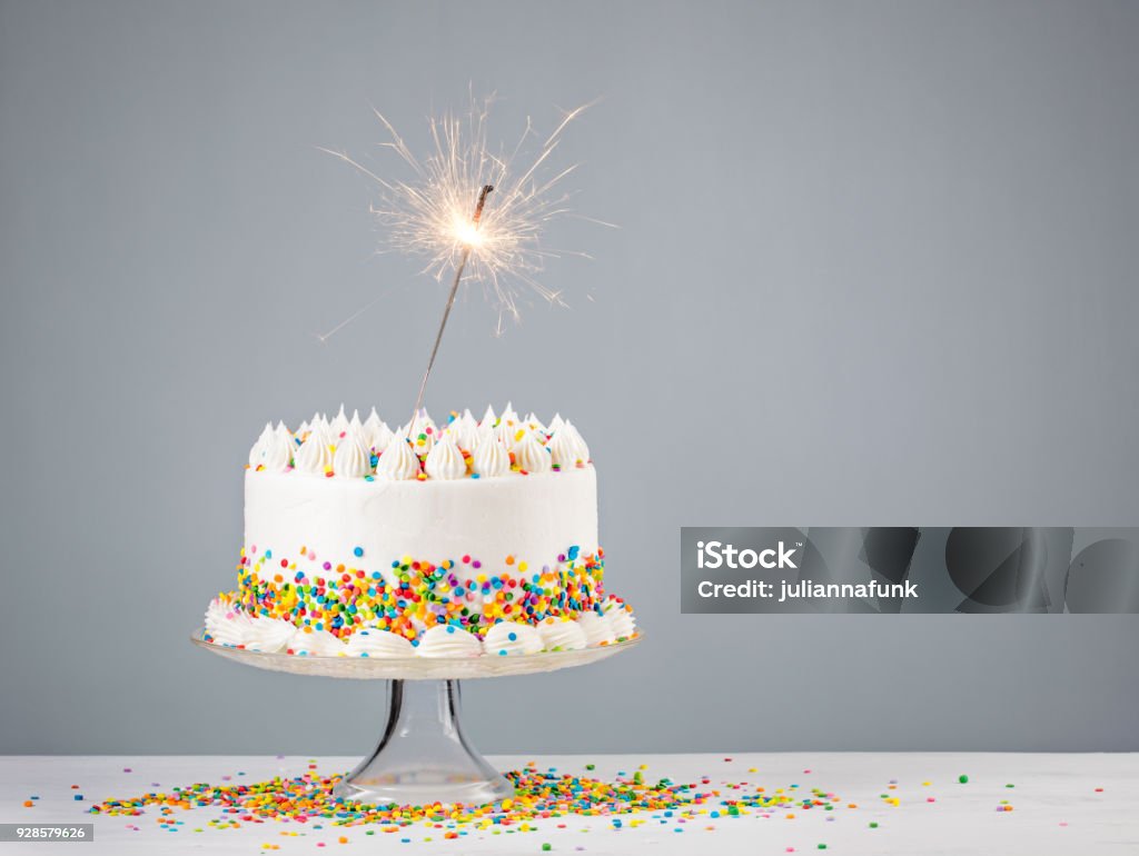 Birthday Cake with Sprinkles White Birthday cake with colorful Sprinkles and sparkler over a neutral background. Birthday Stock Photo