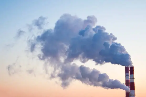 Smoke, fumes coming out of pipes of factory producing heat for central heating in winter on the background of skies.