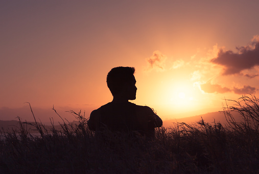 Thoughtful man sitting on grass looking at sunset.