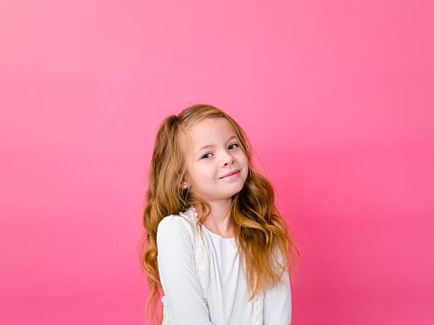 Close up head shot portrait of little brown-haired child girl. Cheerful kid against white studio wall background