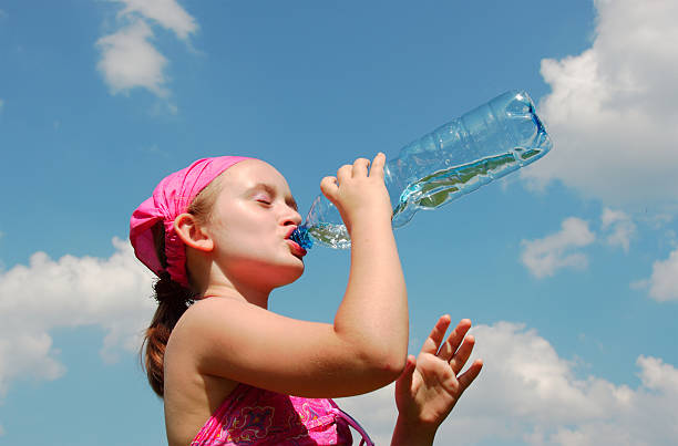Blonde little girl drinking fresh and pure tap water from a glass in a summer garden - healthy lifestyle concept